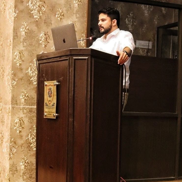 Abid Jamil presenting with a laptop at a wooden lectern