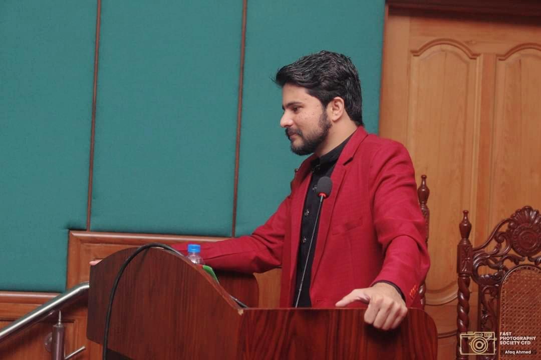 A close-up of Abid Jamil speaking at a lectern at FAST NUCES
