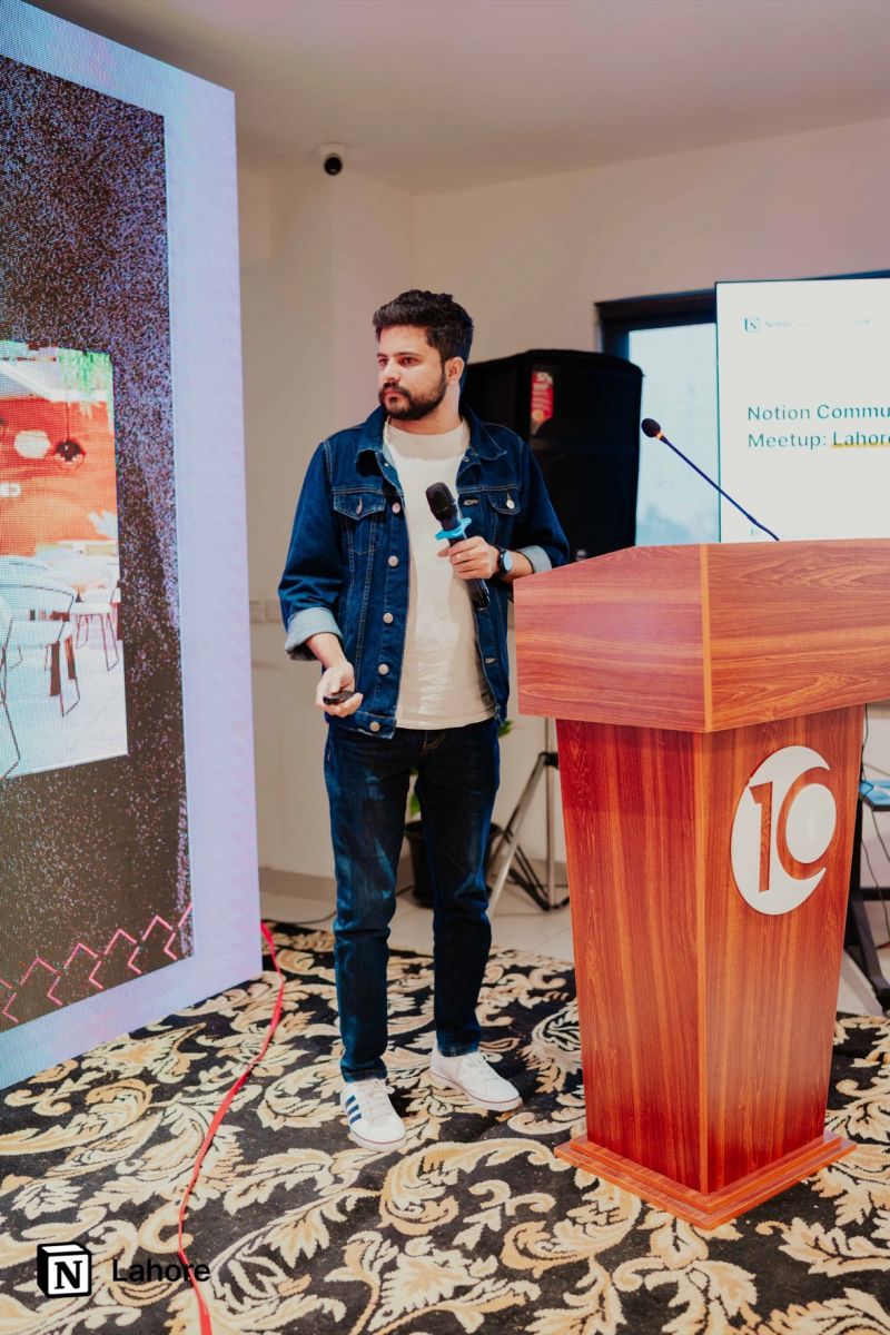 Abid Jamil speaking with a microphone beside a lectern at the Notion Lahore community event